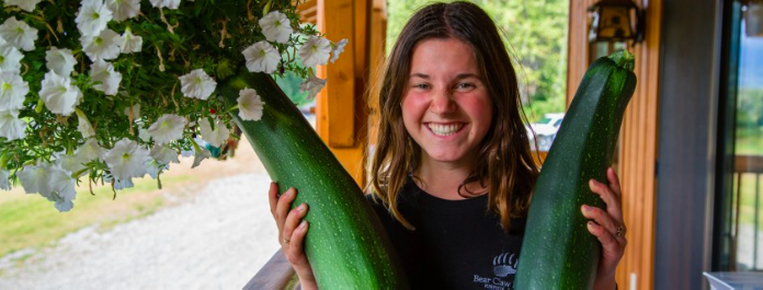 Danielle Bradford holding up some zucchinis grown in the garden at Bear Claw Lodge