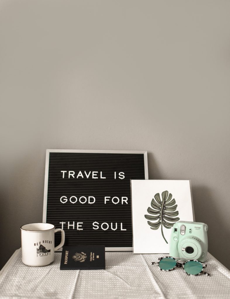 an image of a table with a board that says travel is good for the soul, surrounded by a mug and minimalist artwork