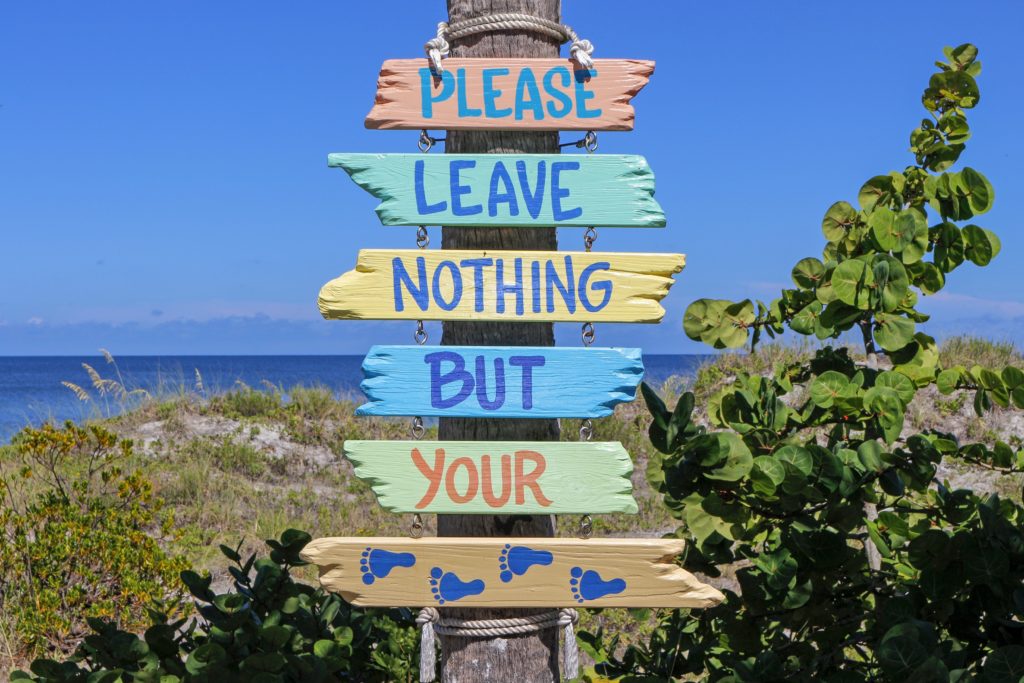 a sign on the beach that depicts a sustainable tourism message, to please leave nothing but your footprints